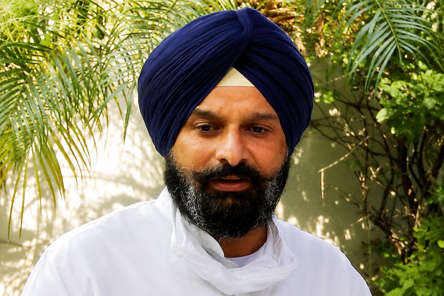 Bikram Singh Majithia at Majitha Police Investigation Sikh political leader wearing a blue turban and white kurta, photographed outdoors during a media interaction surrounded by greenery.