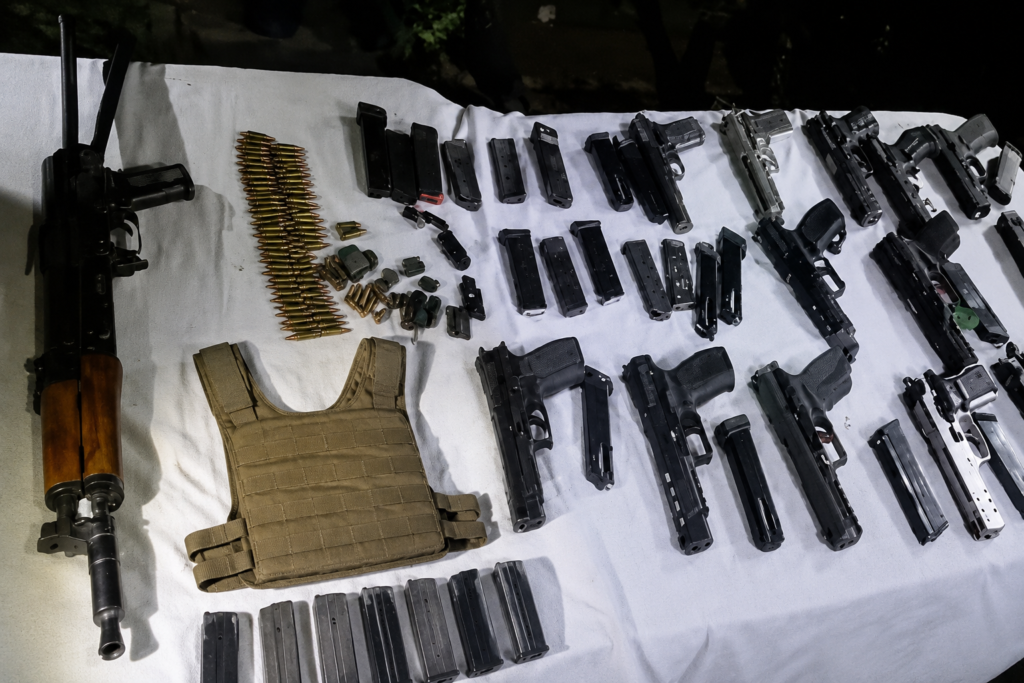Major Arms Cache Recovered Near India-Pakistan Border in Ajnala A large cache of weapons and ammunition recovered by security forces is displayed on a white sheet. The seizure includes an AK-47 rifle, multiple pistols, magazines, live cartridges, and other related items arranged for documentation during a border security operation in Punjab.